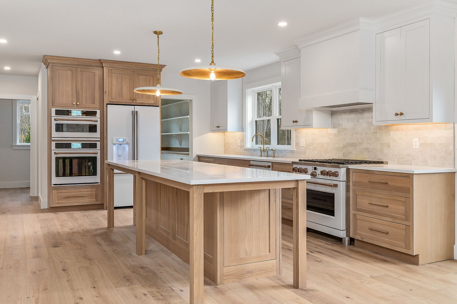 White oak kitchen island with brass pendant lights, stainless range and built-in wall ovens - a River Birch Builders home in the New Hampshire Seacoast