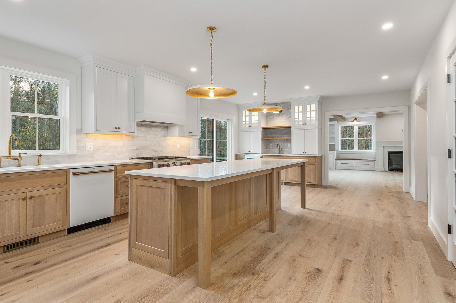 Open kitchen with a long white oak island, brass pendants and wide-plank oak floors - a River Birch Builders home in the New Hampshire Seacoast