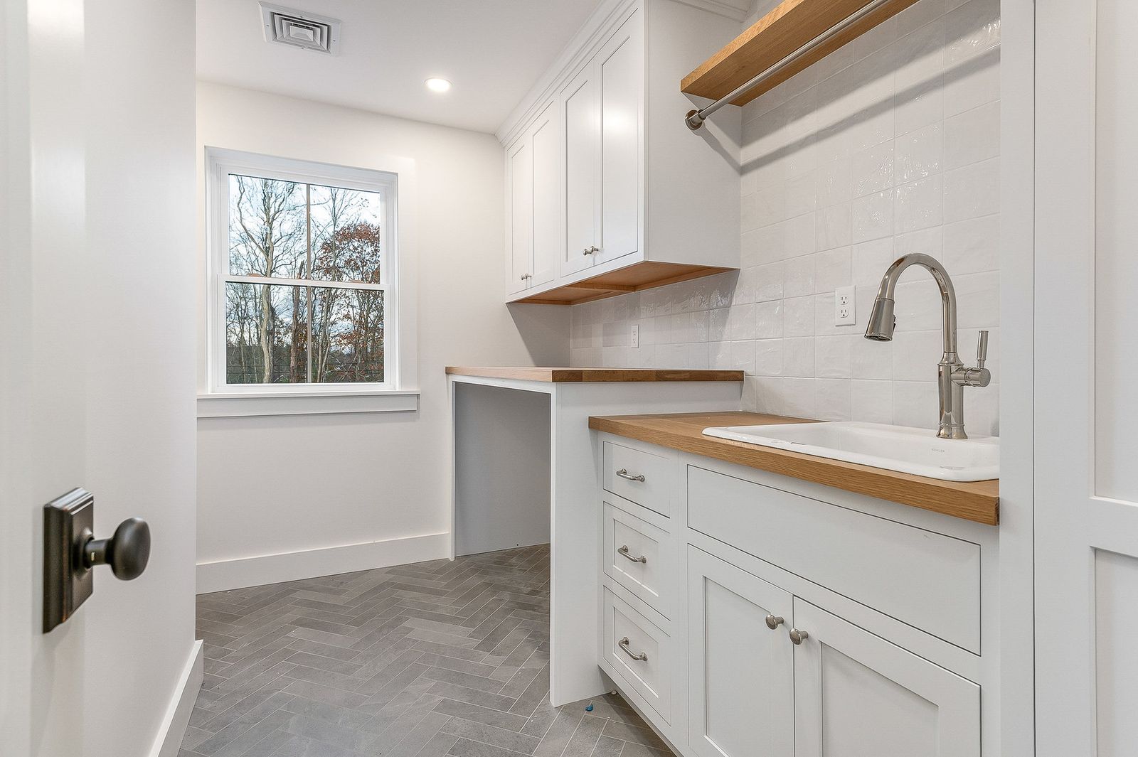 Wet bar with white cabinetry, a floating oak shelf and a brass gooseneck faucet - a River Birch Builders home in the New Hampshire Seacoast