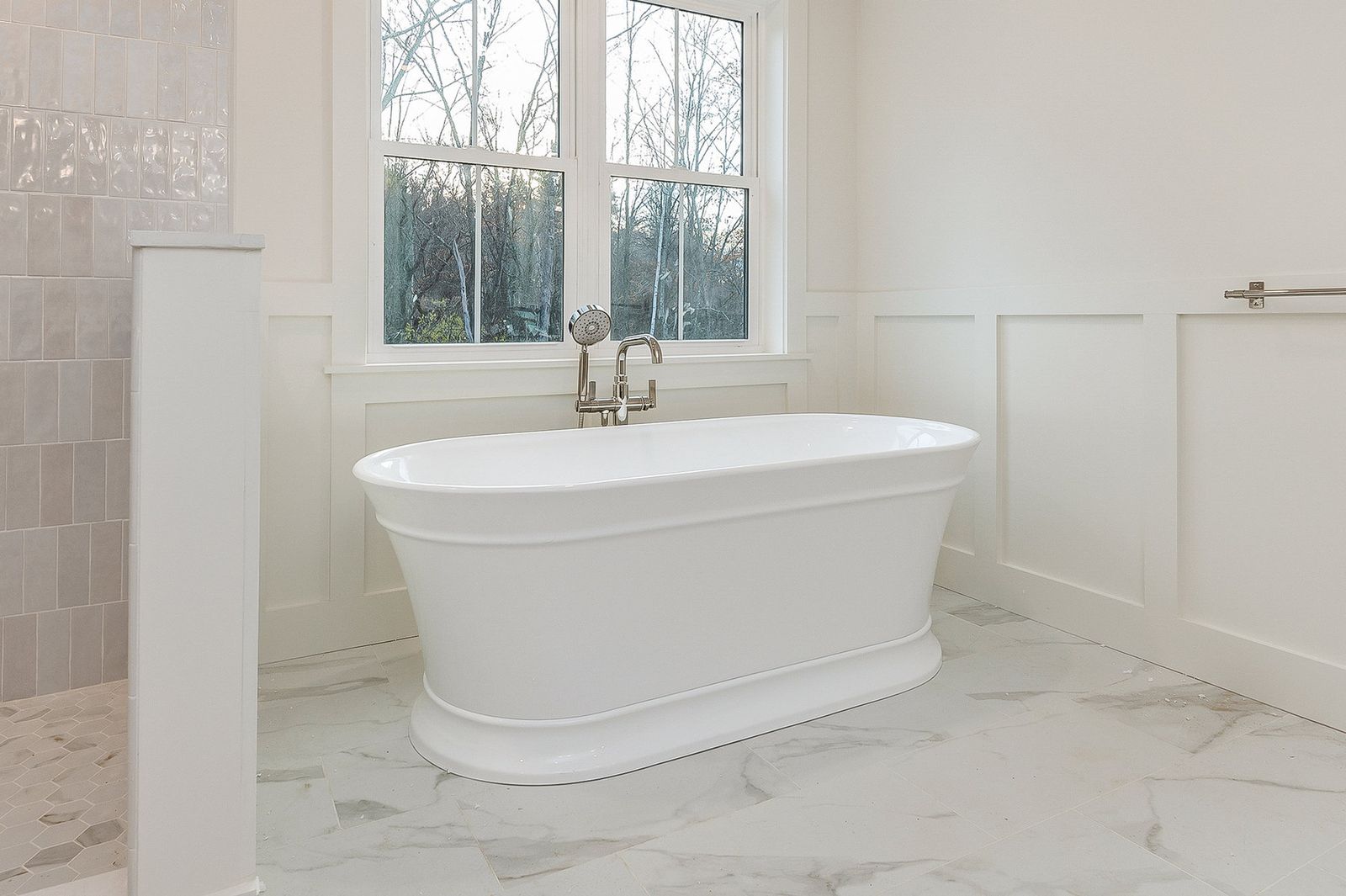 Primary bath with a freestanding soaking tub beneath a window on marble tile - a River Birch Builders home in the New Hampshire Seacoast