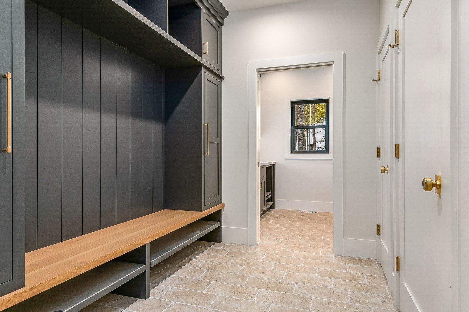 Mudroom with a navy built-in bench, brass hooks and tile flooring - a River Birch Builders home in the New Hampshire Seacoast
