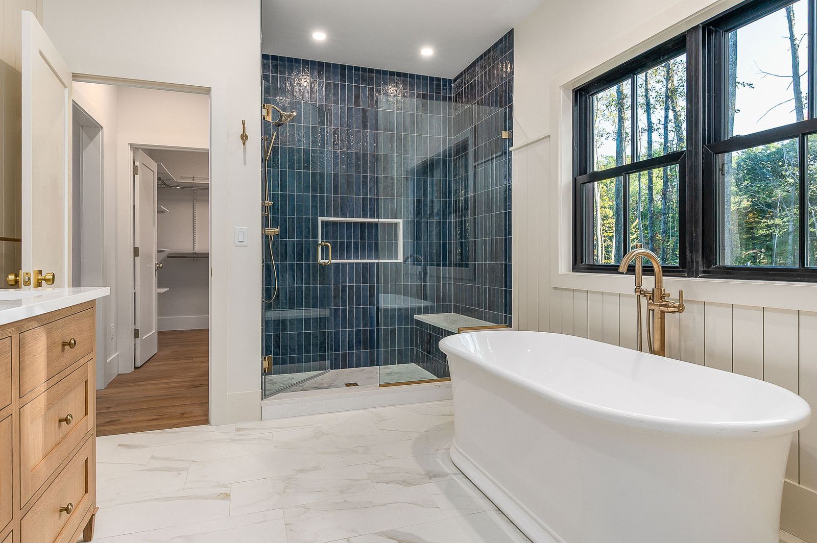 Primary bath with a blue tiled walk-in shower, freestanding tub and brass fixtures - a River Birch Builders home in the New Hampshire Seacoast